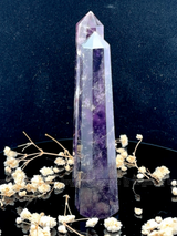 A tall, polished obelisk made of Amethyst, standing upright with smooth, transparent facets that catch and reflect light