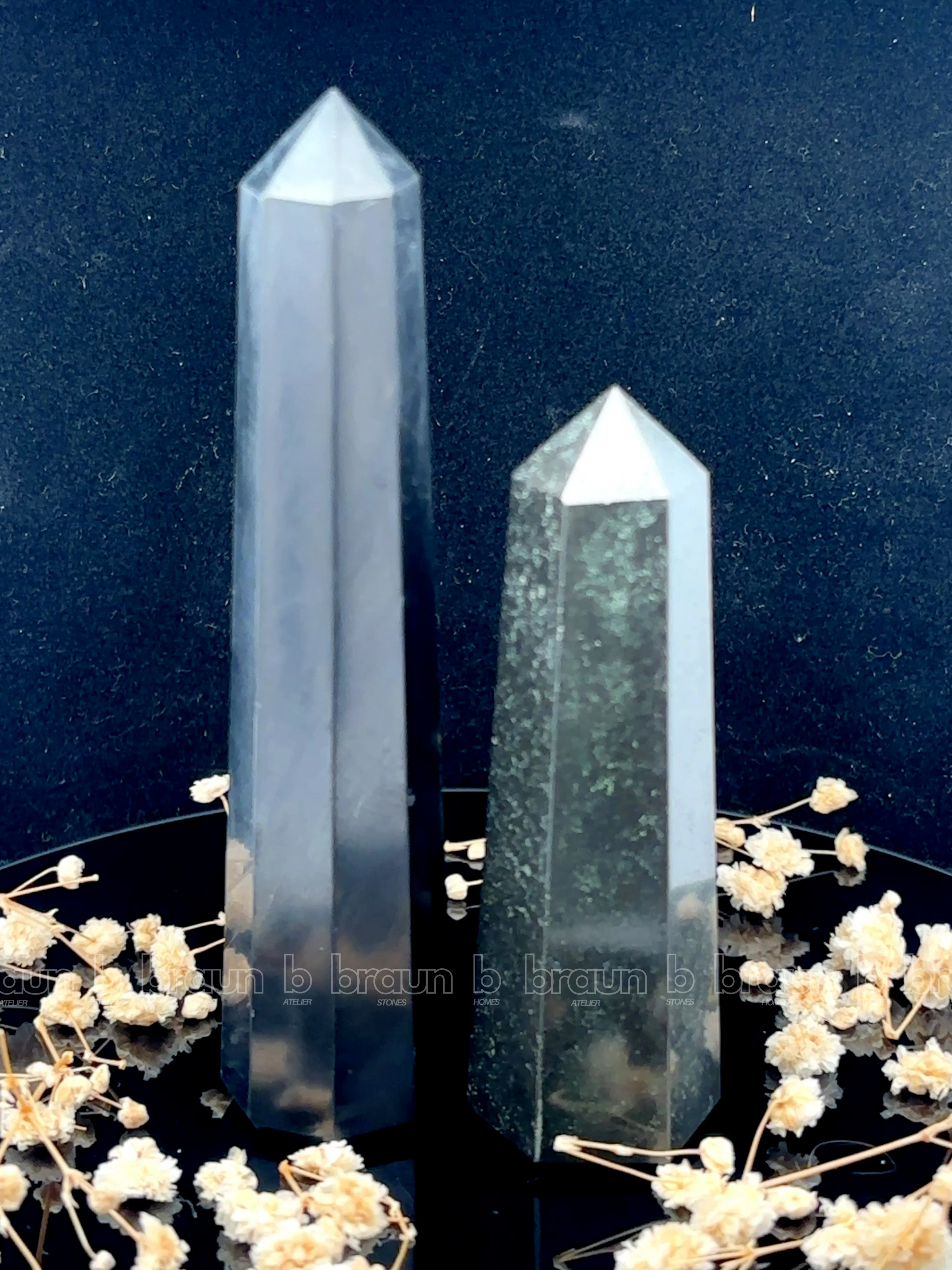A tall, polished obelisk made of Black obsidian, standing upright with smooth, transparent facets that catch and reflect light