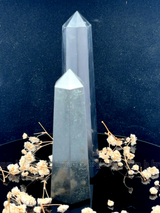 A tall, polished obelisk made of Black obsidian, standing upright with smooth, transparent facets that catch and reflect light