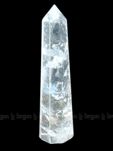 A tall, polished obelisk made of clear quartz crystal, standing upright with smooth, transparent facets that catch and reflect light