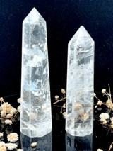 A tall, polished obelisk made of clear quartz crystal, standing upright with smooth, transparent facets that catch and reflect light