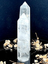 A tall, polished obelisk made of clear quartz crystal, standing upright with smooth, transparent facets that catch and reflect light