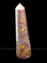 A tall, polished obelisk made of Fruit jasper, standing upright with smooth, transparent facets that catch and reflect light