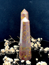 A tall, polished obelisk made of Fruit jasper, standing upright with smooth, transparent facets that catch and reflect light