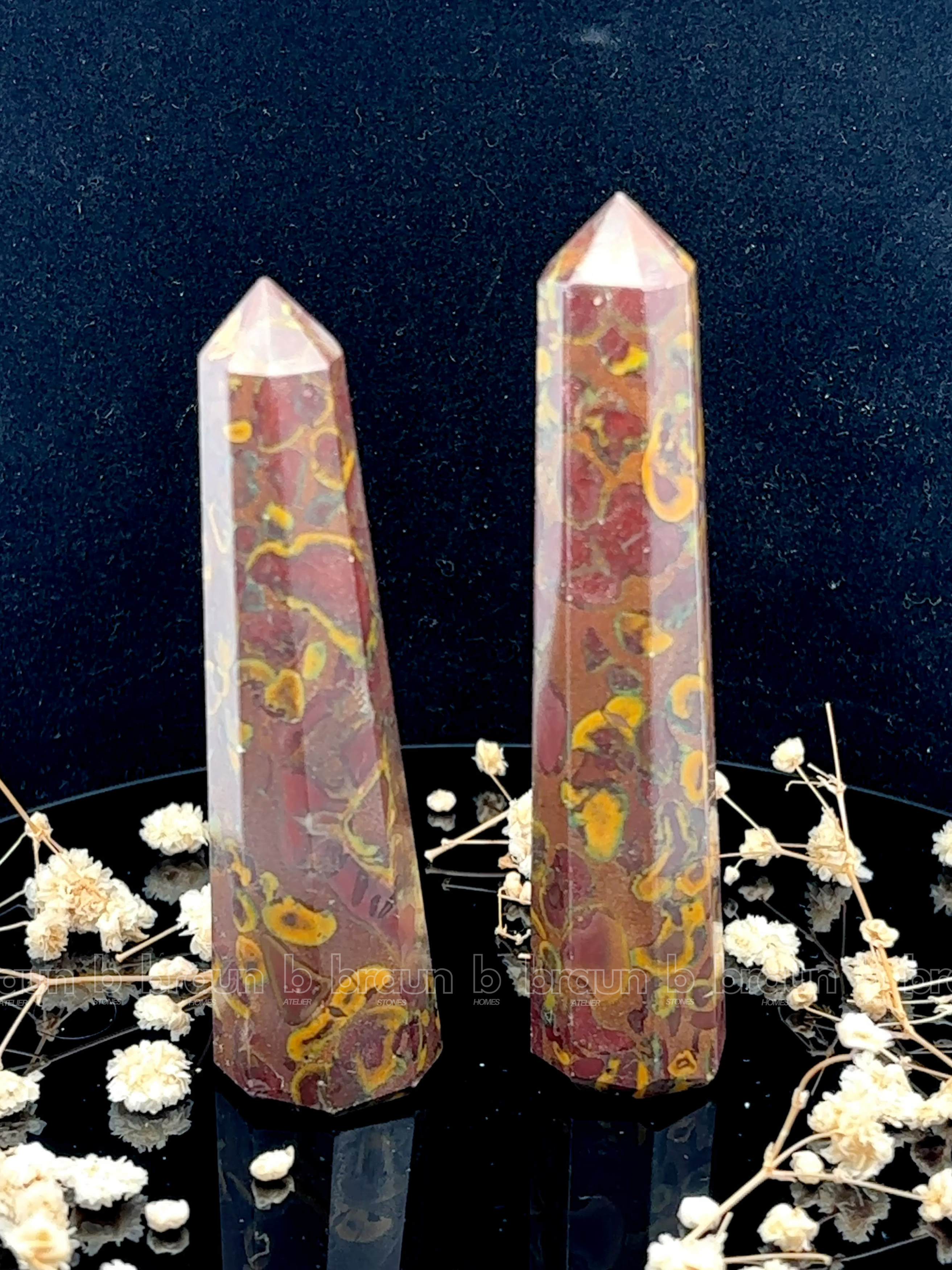 A tall, polished obelisk made of Fruit jasper, standing upright with smooth, transparent facets that catch and reflect light