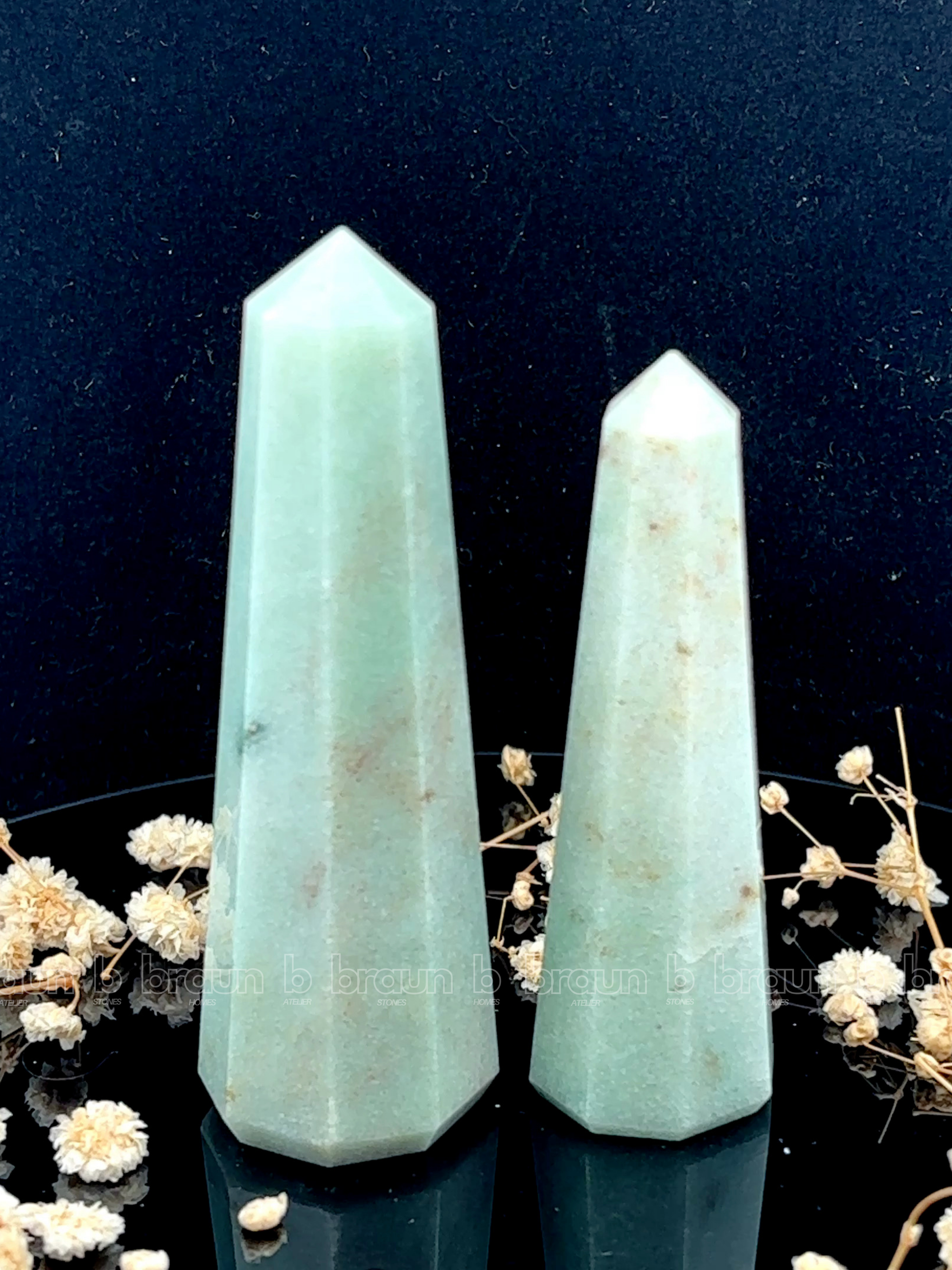 A tall, polished obelisk made of Green aventurine, standing upright with smooth, transparent facets that catch and reflect light
