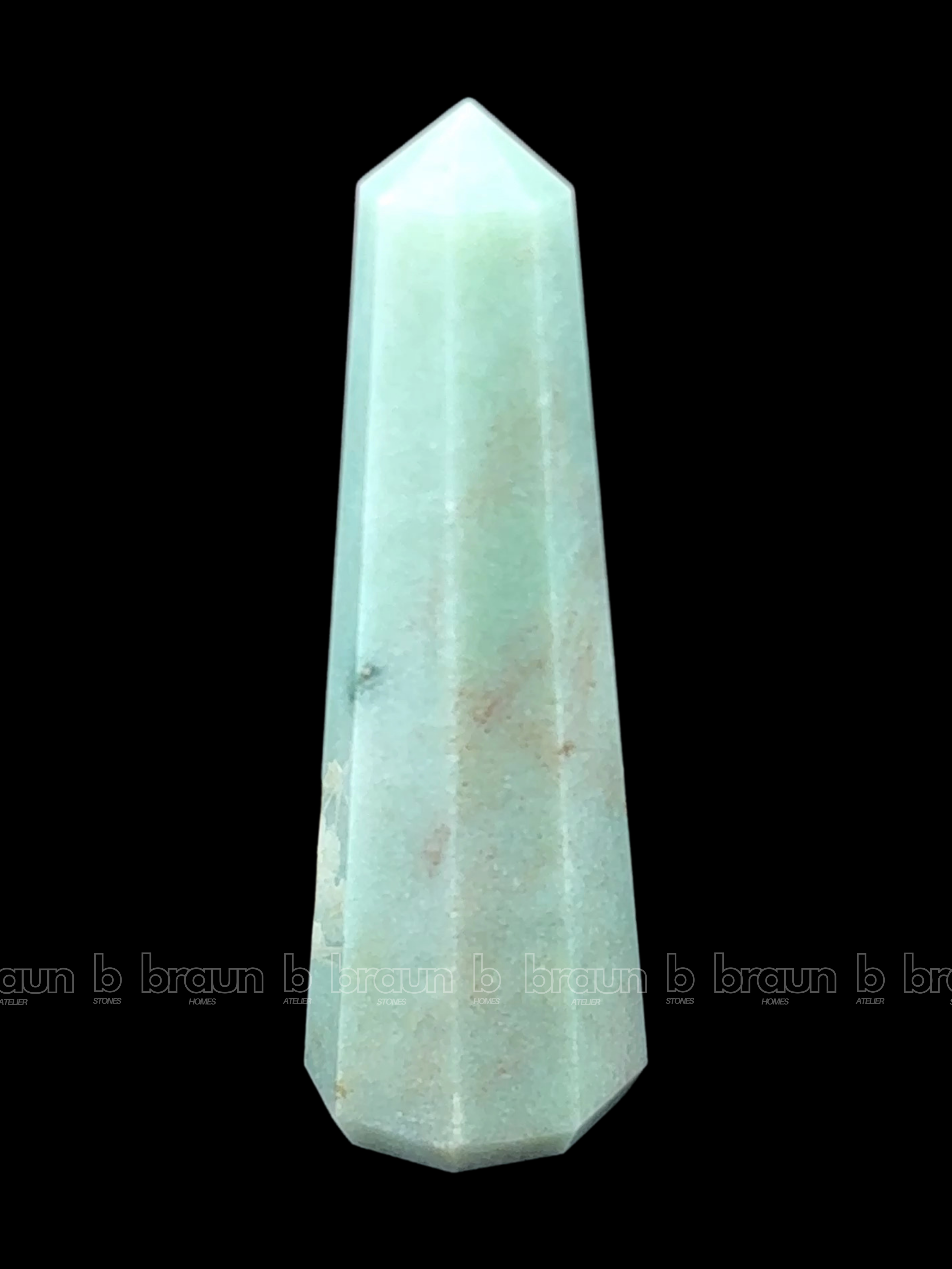 A tall, polished obelisk made of Green aventurine, standing upright with smooth, transparent facets that catch and reflect light