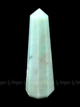 A tall, polished obelisk made of Green aventurine, standing upright with smooth, transparent facets that catch and reflect light