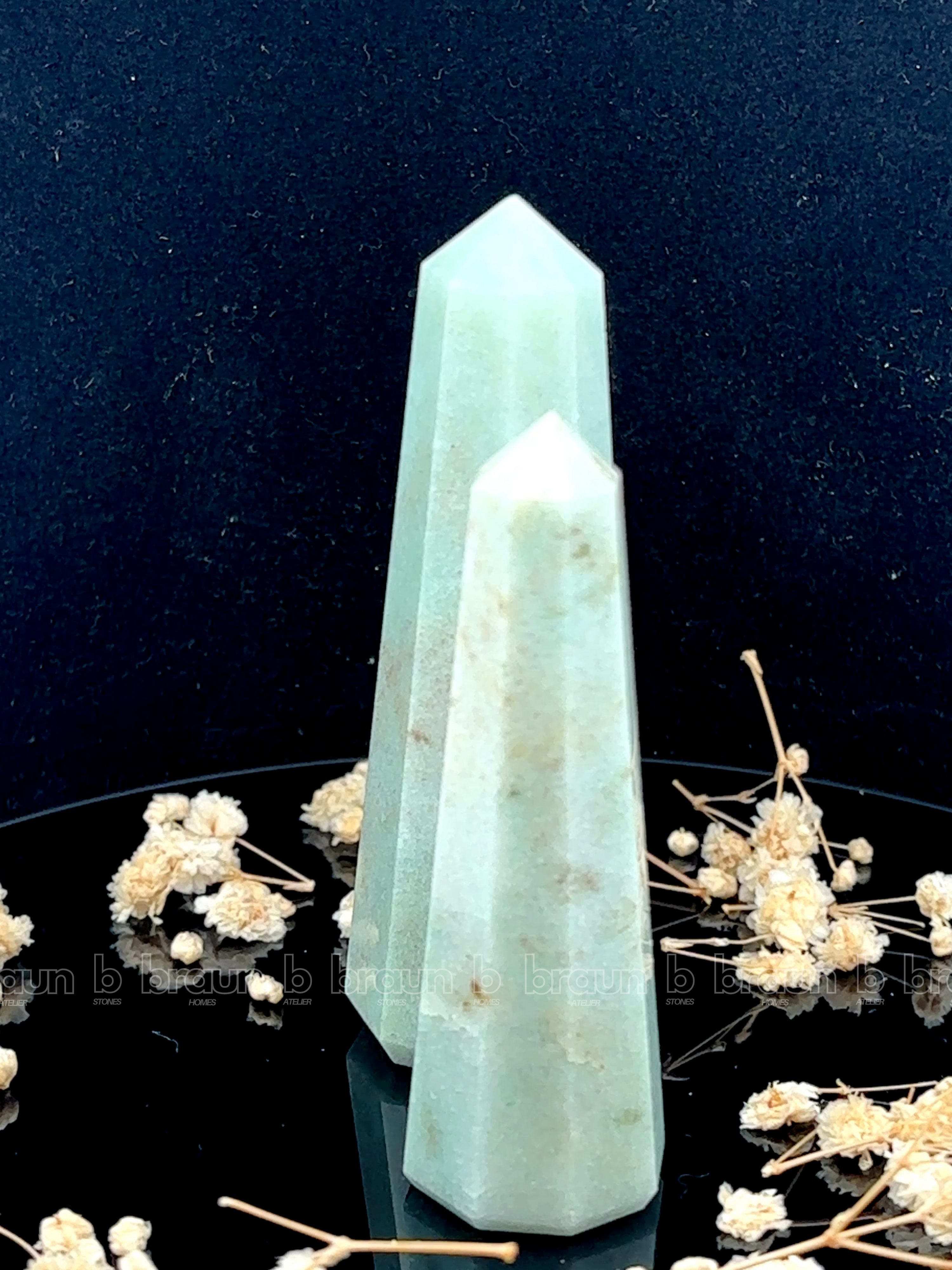 A tall, polished obelisk made of Green aventurine, standing upright with smooth, transparent facets that catch and reflect light