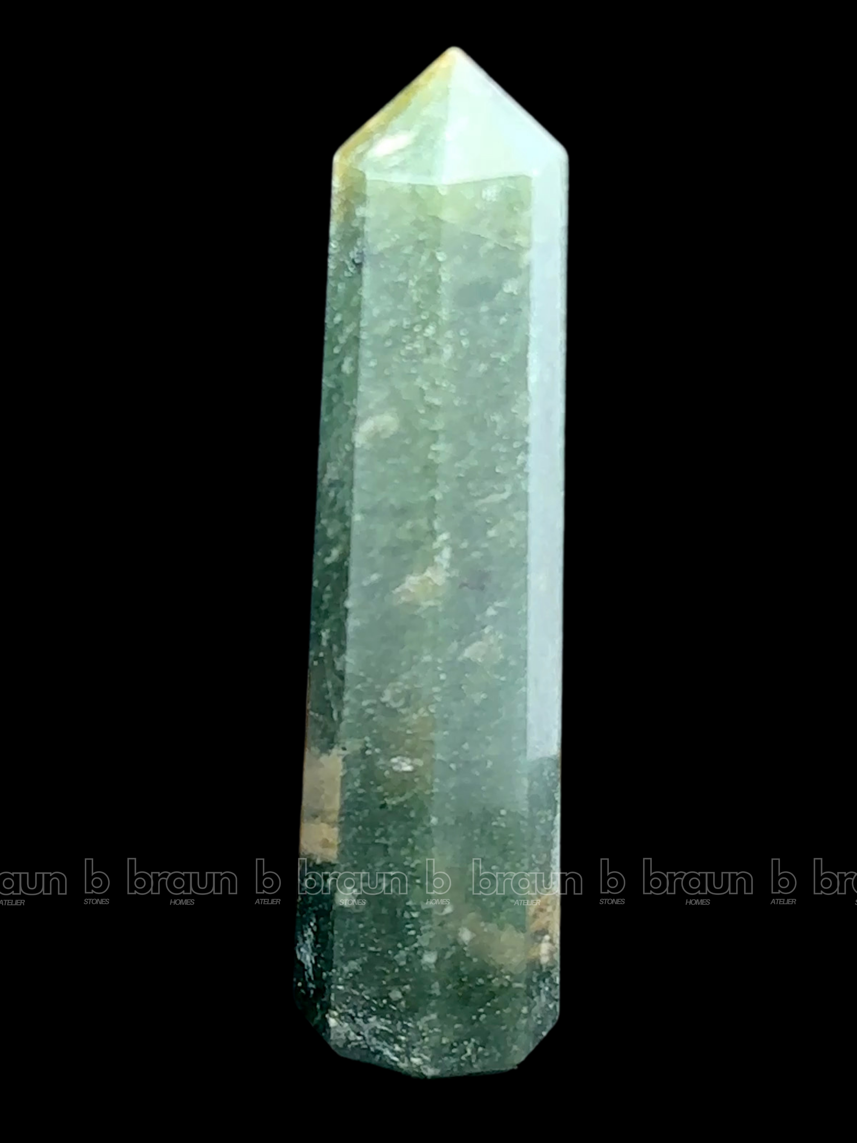 A tall, polished obelisk made of Green mica, standing upright with smooth, transparent facets that catch and reflect light
