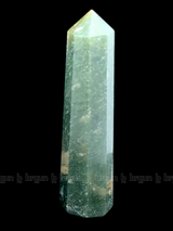 A tall, polished obelisk made of Green mica, standing upright with smooth, transparent facets that catch and reflect light