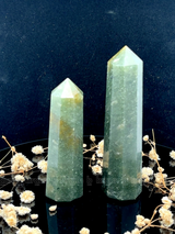 A tall, polished obelisk made of Green mica, standing upright with smooth, transparent facets that catch and reflect light