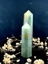 A tall, polished obelisk made of Green mica, standing upright with smooth, transparent facets that catch and reflect light