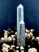 A tall, polished obelisk made of Hematite, standing upright with smooth, transparent facets that catch and reflect light
