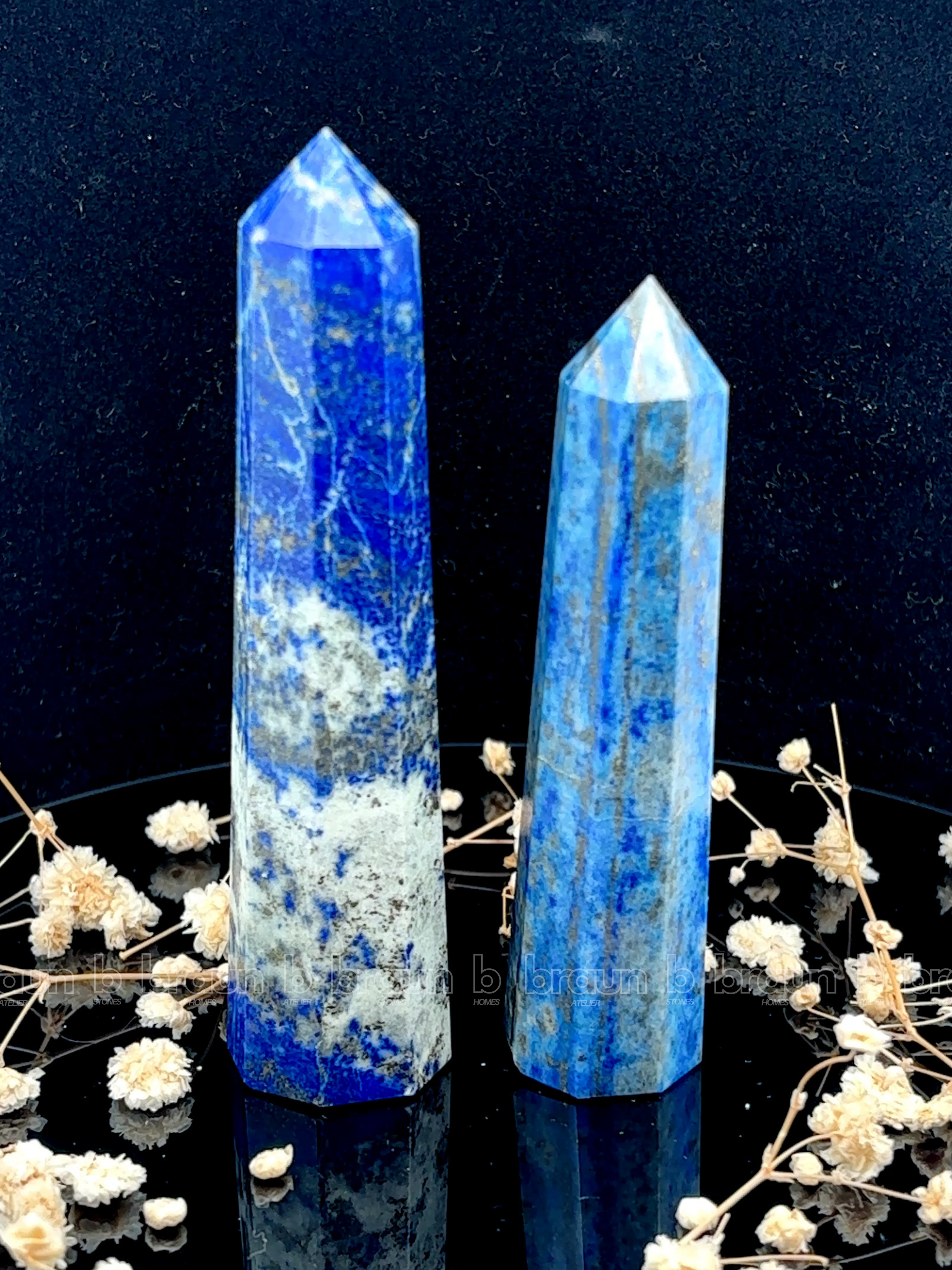 A tall, polished obelisk made of Lapiz lazuli, standing upright with smooth, transparent facets that catch and reflect light