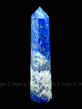 A tall, polished obelisk made of Lapiz lazuli, standing upright with smooth, transparent facets that catch and reflect light