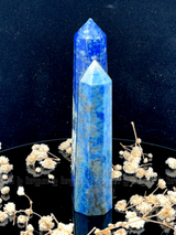 A tall, polished obelisk made of Lapiz lazuli, standing upright with smooth, transparent facets that catch and reflect light
