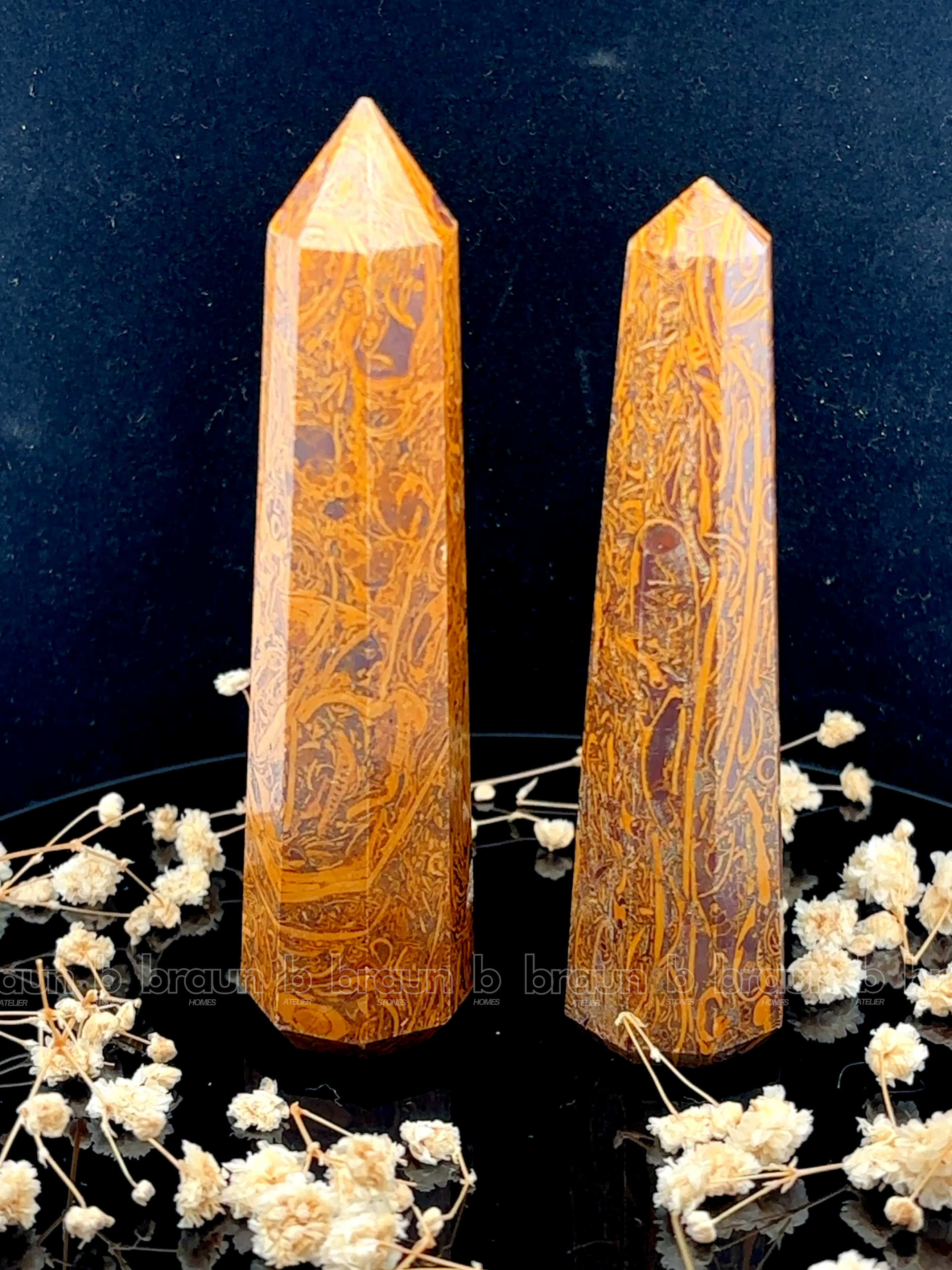 A tall, polished obelisk made of Mariam Jasper, standing upright with smooth, transparent facets that catch and reflect light