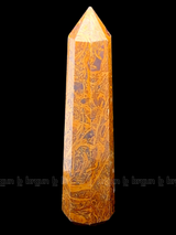 A tall, polished obelisk made of Mariam Jasper, standing upright with smooth, transparent facets that catch and reflect light