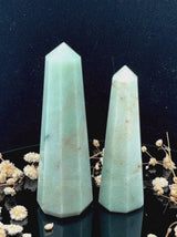 A tall, polished obelisk made of Green aventurine, standing upright with smooth, transparent facets that catch and reflect light