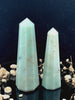 A tall, polished obelisk made of Green aventurine, standing upright with smooth, transparent facets that catch and reflect light