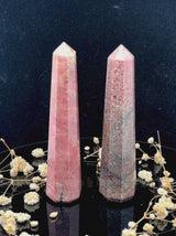 A tall, polished obelisk made of Rhodonite, standing upright with smooth, transparent facets that catch and reflect light