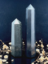 A tall, polished obelisk made of Black obsidian, standing upright with smooth, transparent facets that catch and reflect light