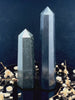 A tall, polished obelisk made of Black obsidian, standing upright with smooth, transparent facets that catch and reflect light