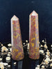 A tall, polished obelisk made of Fruit jasper, standing upright with smooth, transparent facets that catch and reflect light
