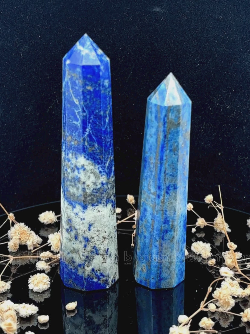 A tall, polished obelisk made of Lapiz lazuli, standing upright with smooth, transparent facets that catch and reflect light