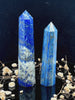 A tall, polished obelisk made of Lapiz lazuli, standing upright with smooth, transparent facets that catch and reflect light