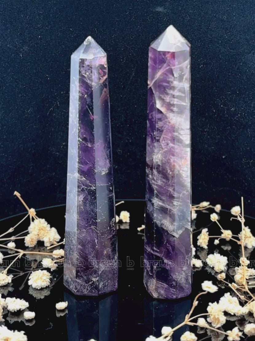 A tall, polished obelisk made of Amethyst, standing upright with smooth, transparent facets that catch and reflect light