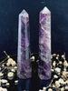A tall, polished obelisk made of Amethyst, standing upright with smooth, transparent facets that catch and reflect light