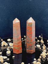 A tall, polished obelisk made of Unakite, standing upright with smooth, transparent facets that catch and reflect light