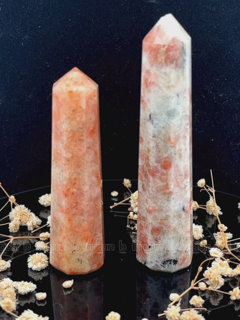 A tall, polished obelisk made of Sunstone, standing upright with smooth, transparent facets that catch and reflect light