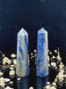 A tall, polished obelisk made of Sodalite, standing upright with smooth, transparent facets that catch and reflect light