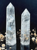 A tall, polished obelisk made of clear quartz crystal, standing upright with smooth, transparent facets that catch and reflect light