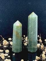 A tall, polished obelisk made of Green mica, standing upright with smooth, transparent facets that catch and reflect light