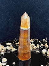 A tall, polished obelisk made of Yellow Fluorite, standing upright with smooth, transparent facets that catch and reflect light
