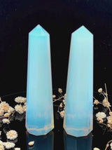 A tall, polished obelisk made of Opal, standing upright with smooth, transparent facets that catch and reflect light