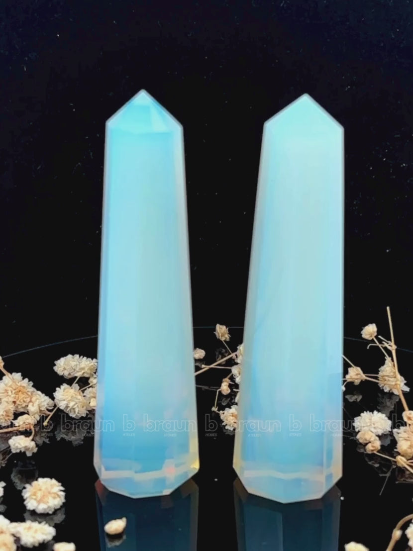 A tall, polished obelisk made of Opal, standing upright with smooth, transparent facets that catch and reflect light