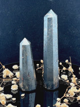 A tall, polished obelisk made of Hematite, standing upright with smooth, transparent facets that catch and reflect light