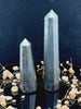A tall, polished obelisk made of Hematite, standing upright with smooth, transparent facets that catch and reflect light