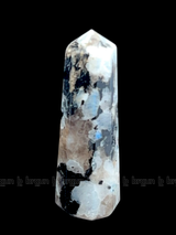 A tall, polished obelisk made of Rainbow Moonstone, standing upright with smooth, transparent facets that catch and reflect light