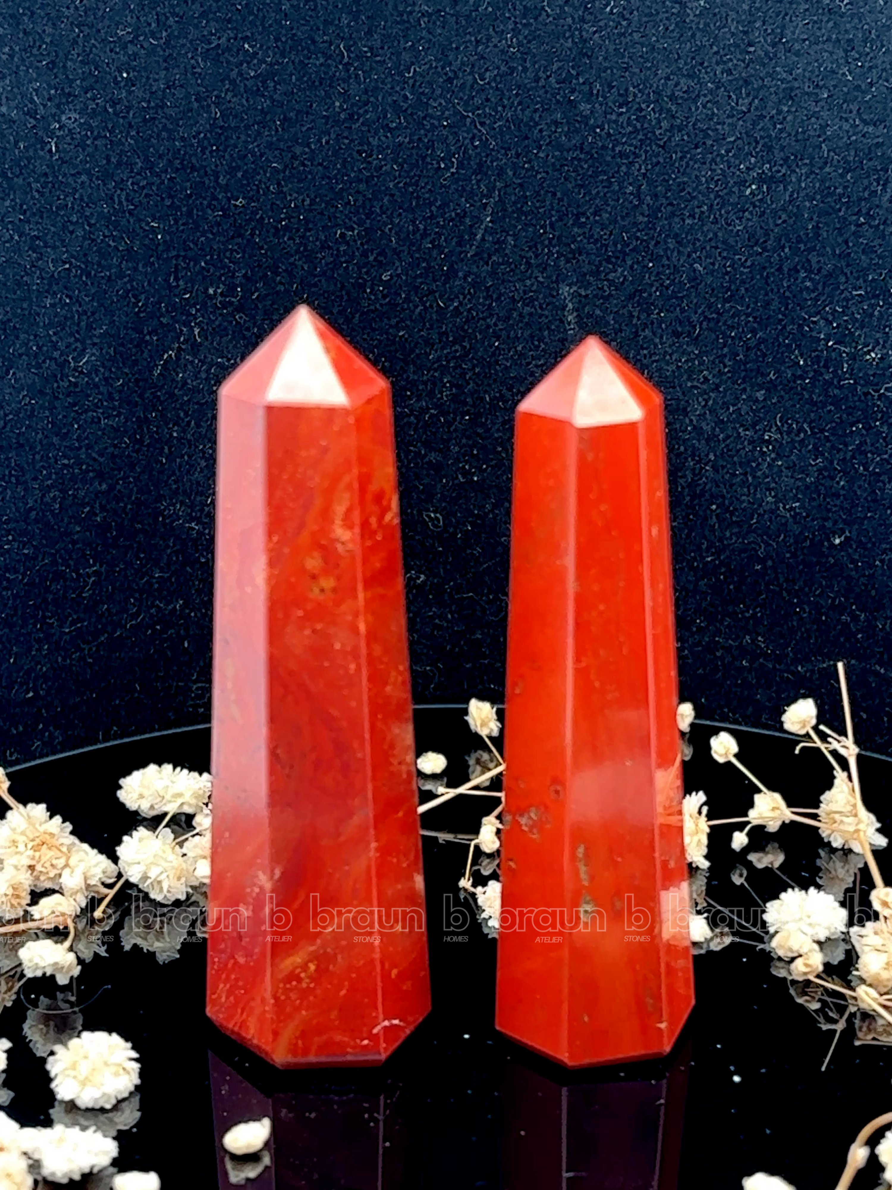 A tall, polished obelisk made of Red Jasper, standing upright with smooth, transparent facets that catch and reflect light