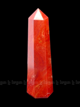 A tall, polished obelisk made of Red Jasper, standing upright with smooth, transparent facets that catch and reflect light