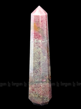 A tall, polished obelisk made of Rhodonite, standing upright with smooth, transparent facets that catch and reflect light