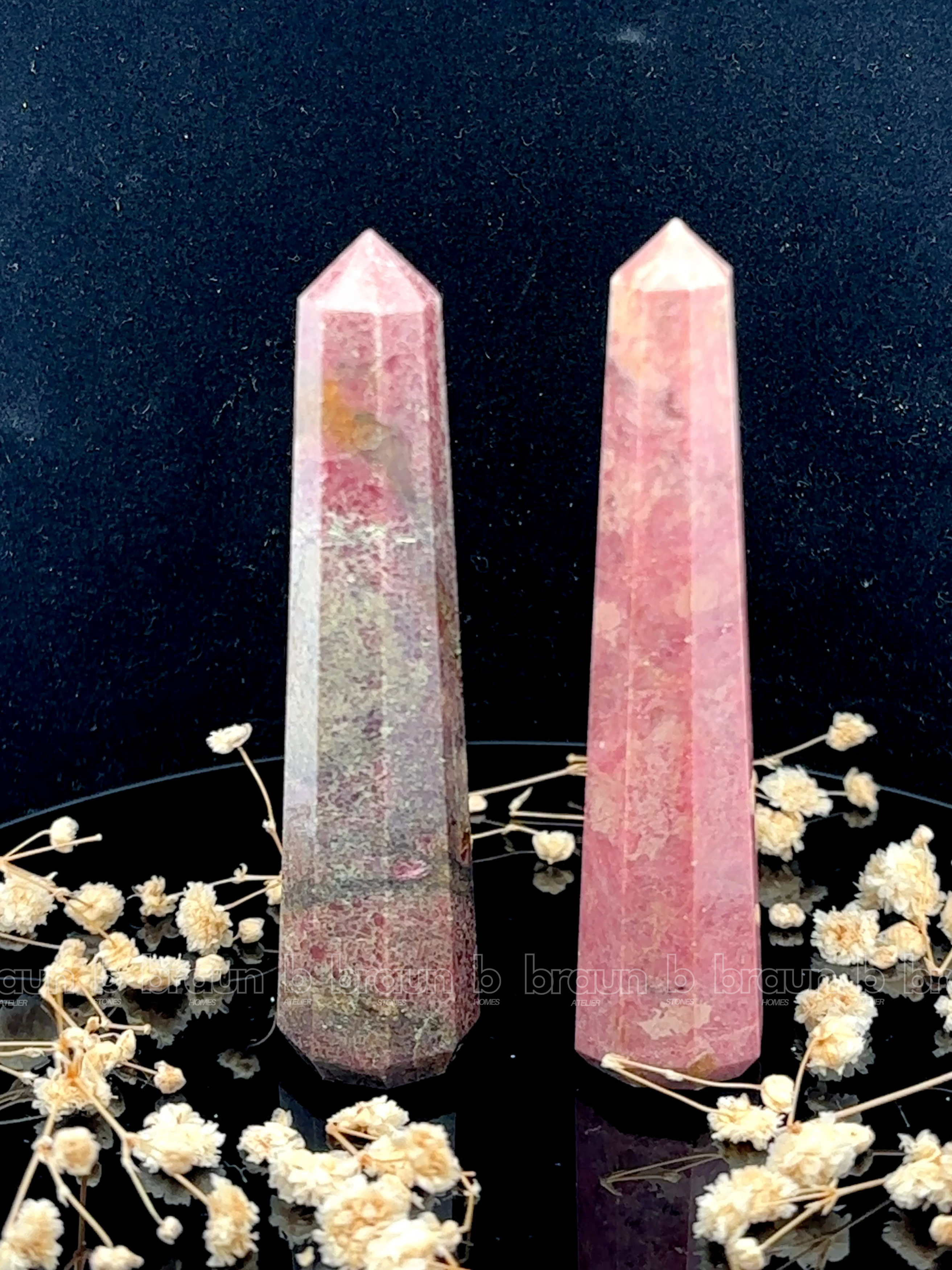 A tall, polished obelisk made of Rhodonite, standing upright with smooth, transparent facets that catch and reflect light