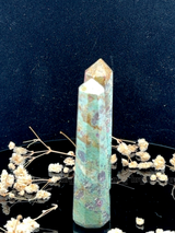 A tall, polished obelisk made of Ruby Fuchsite, standing upright with smooth, transparent facets that catch and reflect light