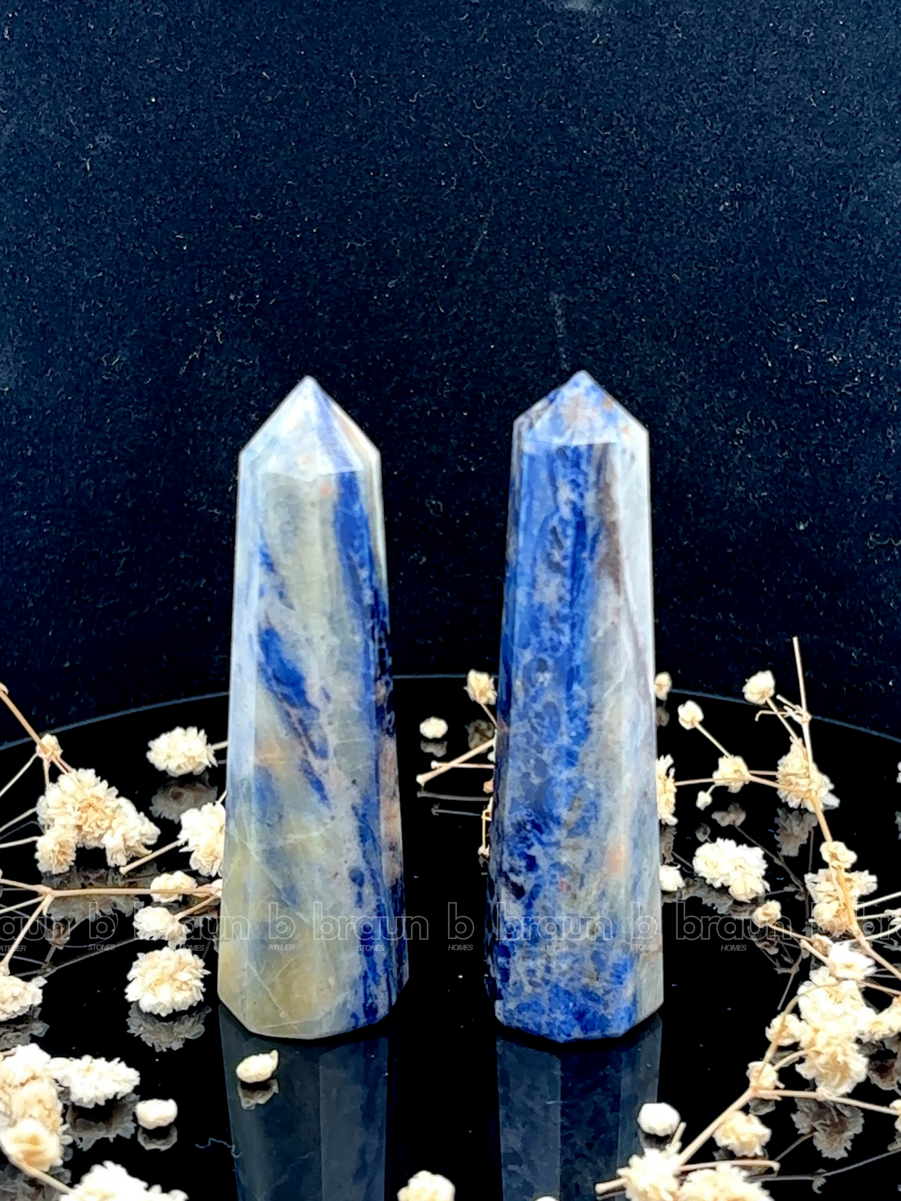A tall, polished obelisk made of Sodalite, standing upright with smooth, transparent facets that catch and reflect light